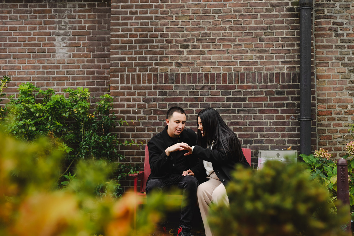 Recently engaged couple sitting together in a quiet Amsterdam courtyard while admiring the engagement ring.