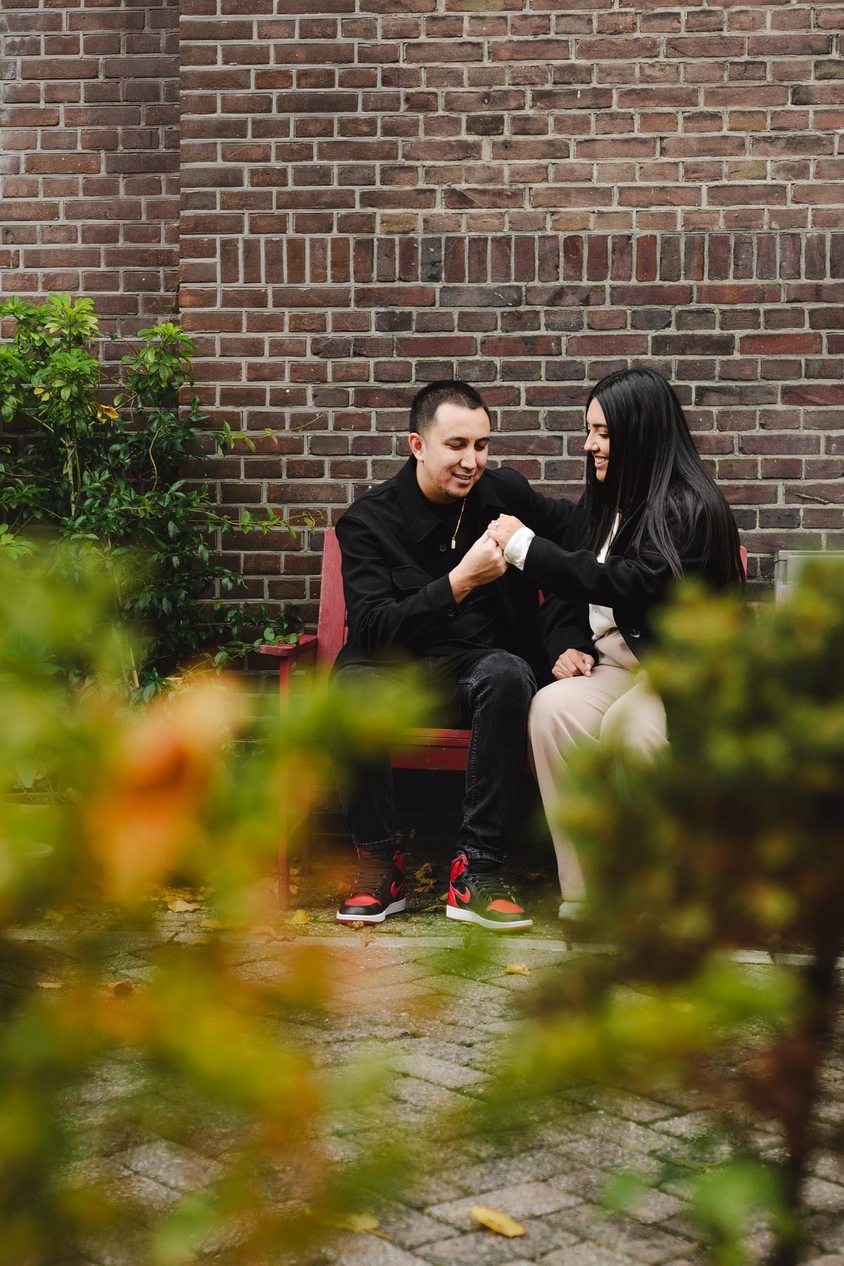Recently engaged couple sitting together in a quiet Amsterdam courtyard while admiring the engagement ring.