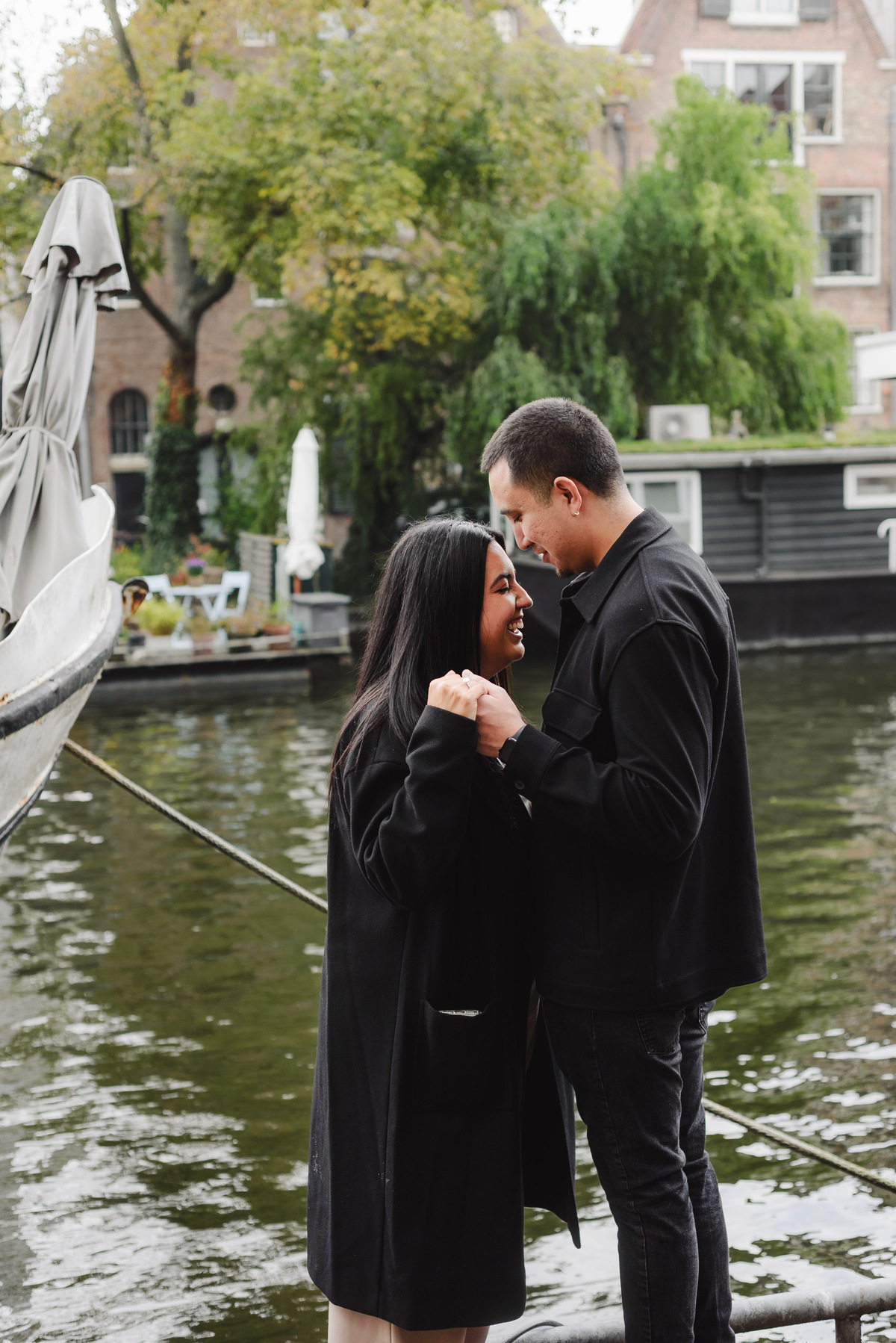 Engaged couple standing on a bridge overlooking Brouwersgracht canal surrounded by bicycles and historic Amsterdam architecture.