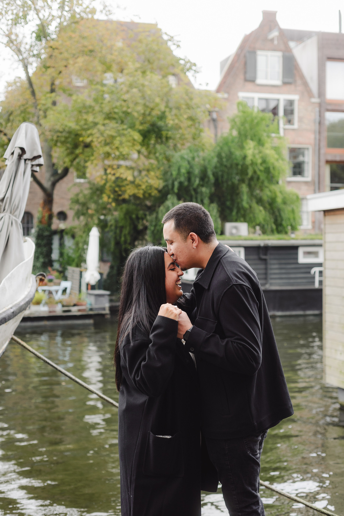 Engaged couple standing on a bridge overlooking Brouwersgracht canal surrounded by bicycles and historic Amsterdam architecture.