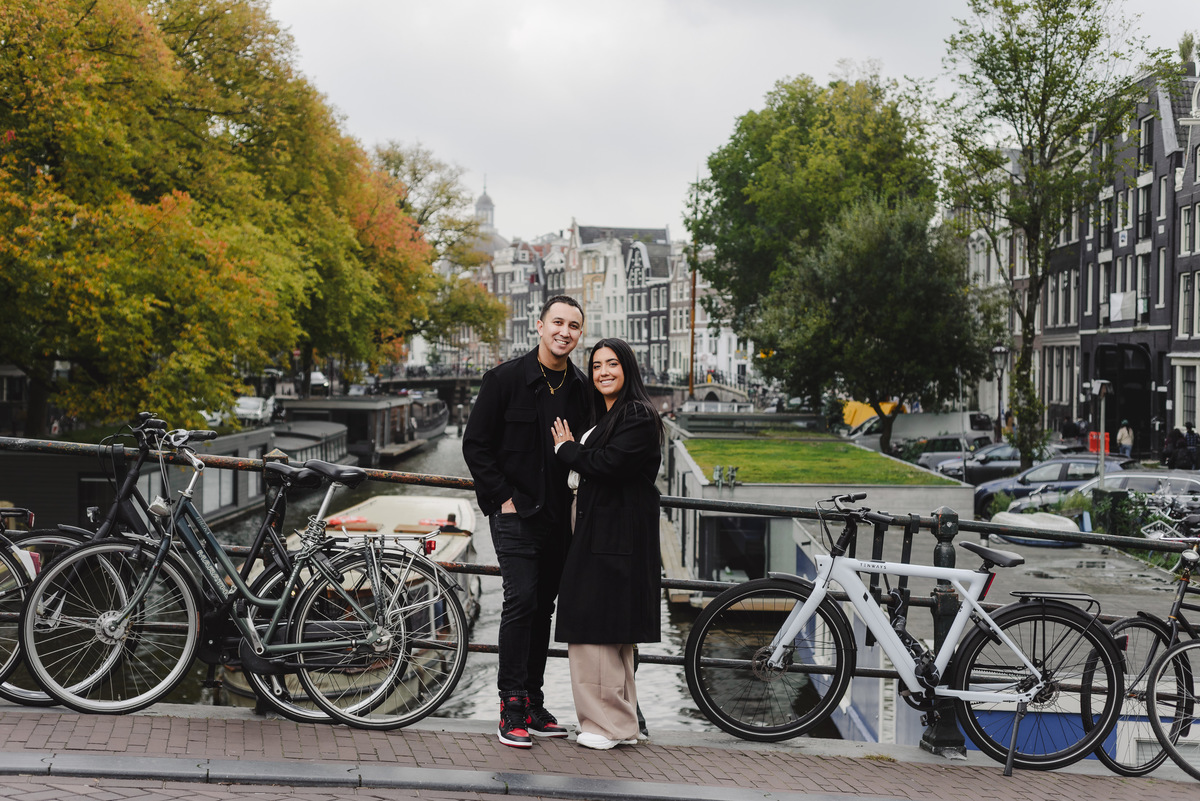 Recently engaged couple posing on Brouwersgracht surrounded by bicycles, canal views, and traditional Amsterdam architecture.