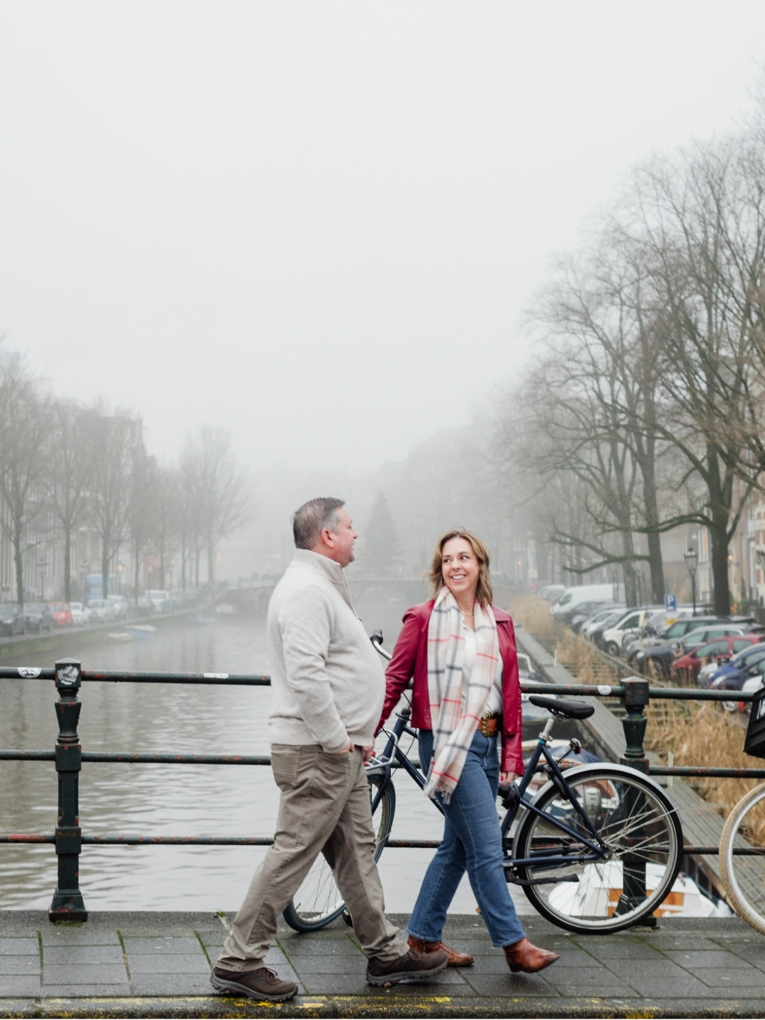 Couple walking together beside a misty Amsterdam canal lined with bicycles and historic houses.