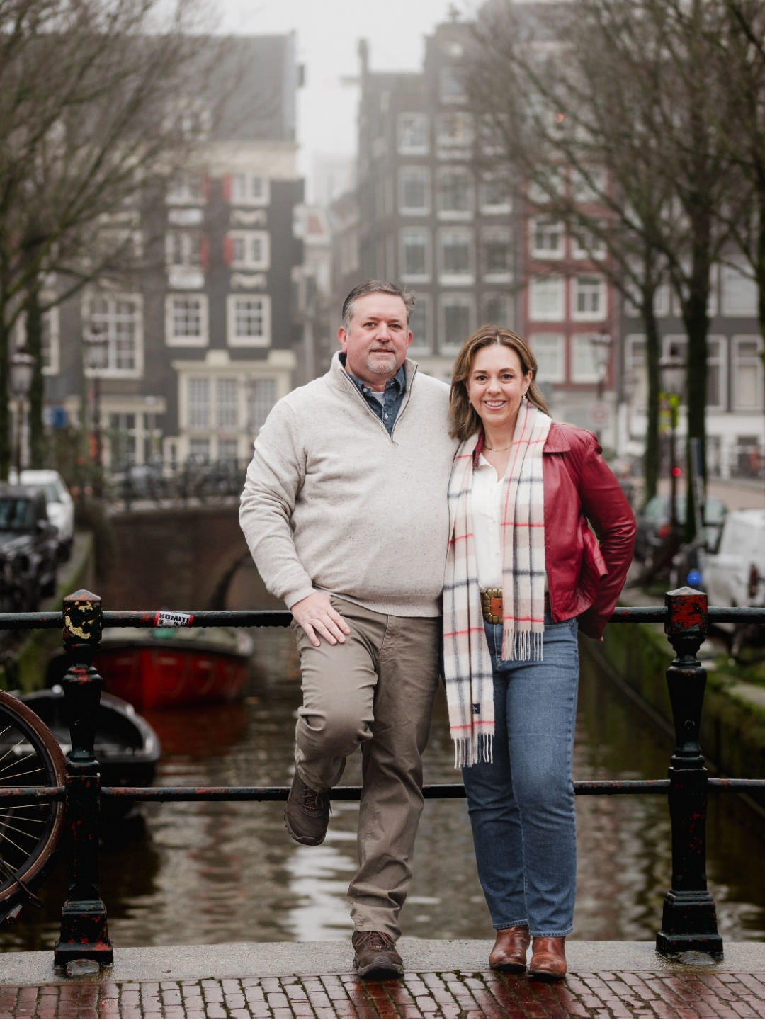 Couple embracing on an Amsterdam bridge overlooking a historic canal on a foggy morning.