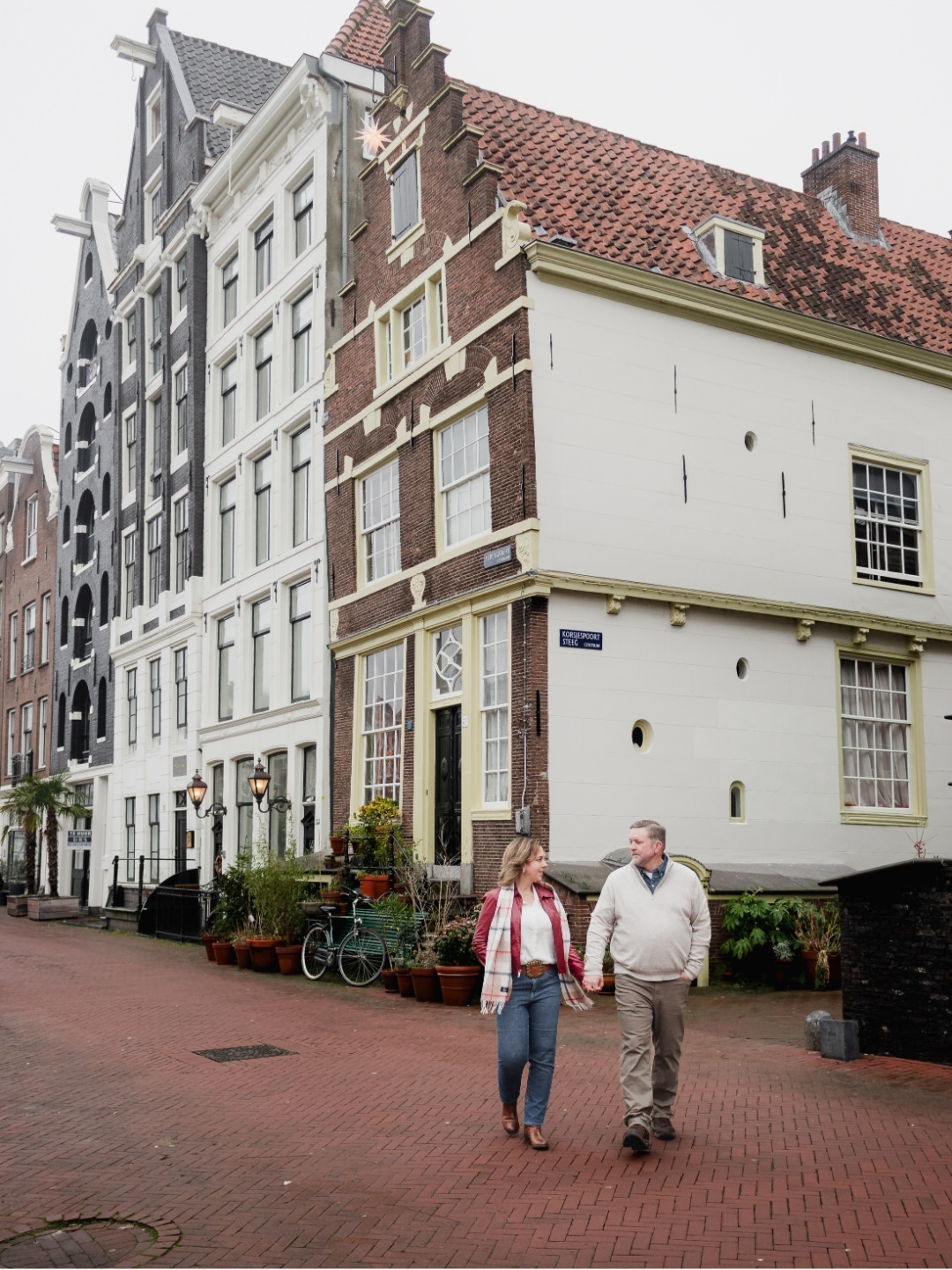Couple walking hand in hand beside a historic canal house in Amsterdam's Canal Belt.