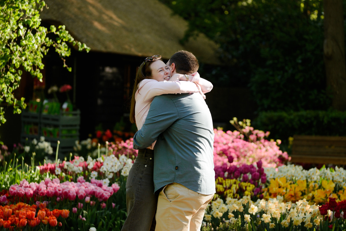 Couple embracing moments after a surprise proposal surrounded by blooming tulips