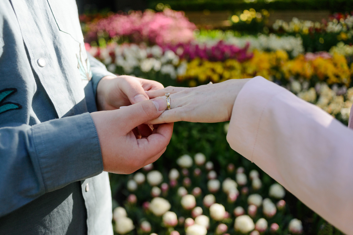 Close-up photograph of an engagement ring being placed on a hand among spring flowers.