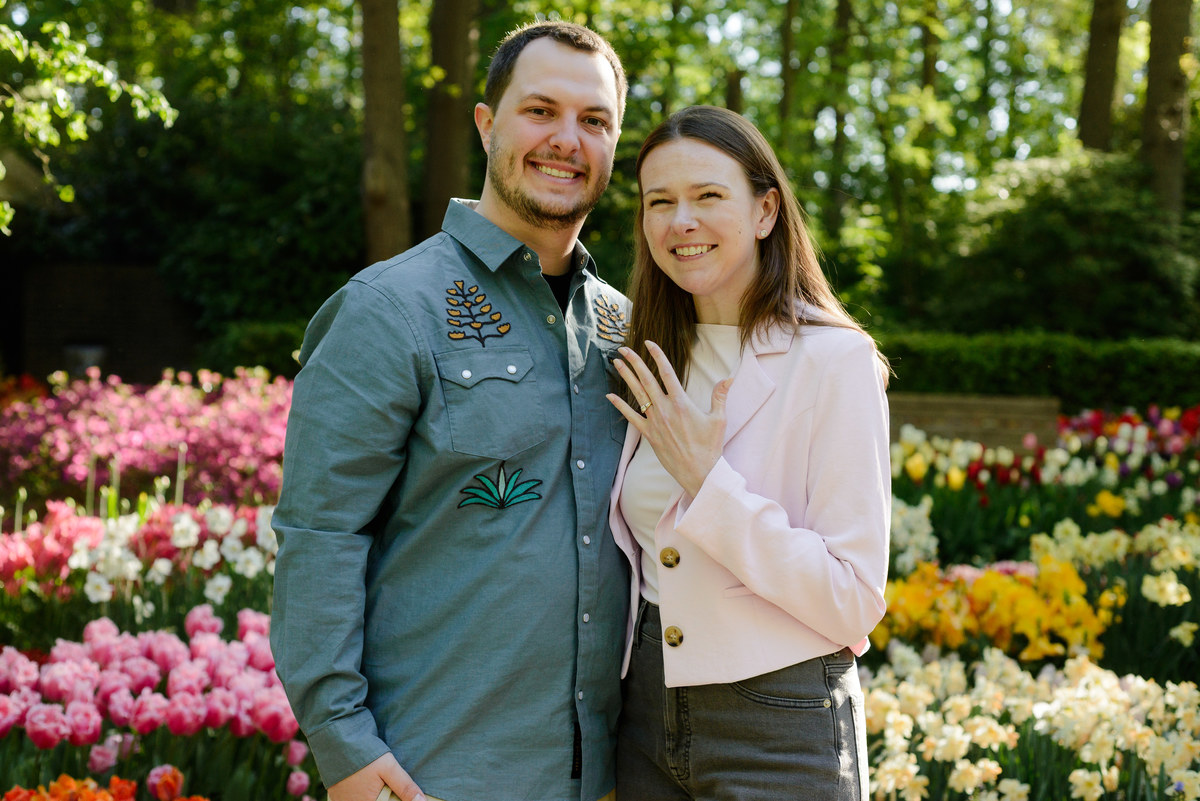 Newly engaged couple smiling among colorful tulip displays at Keukenhof Gardens.
