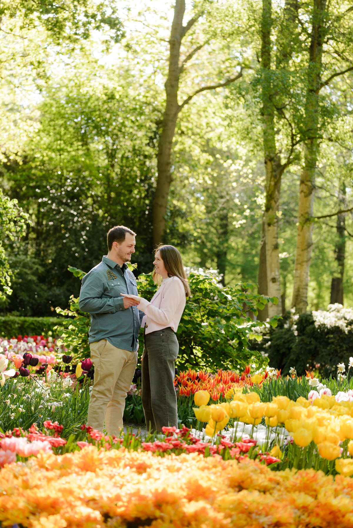 Couple standing together near the proposal location surrounded by flowers and trees.