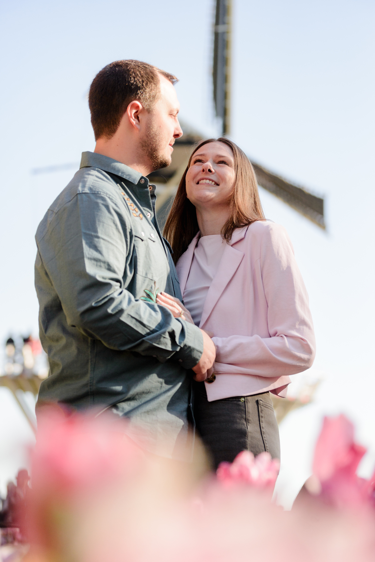 Newly engaged couple walking through Keukenhof Gardens near the iconic Dutch windmill.