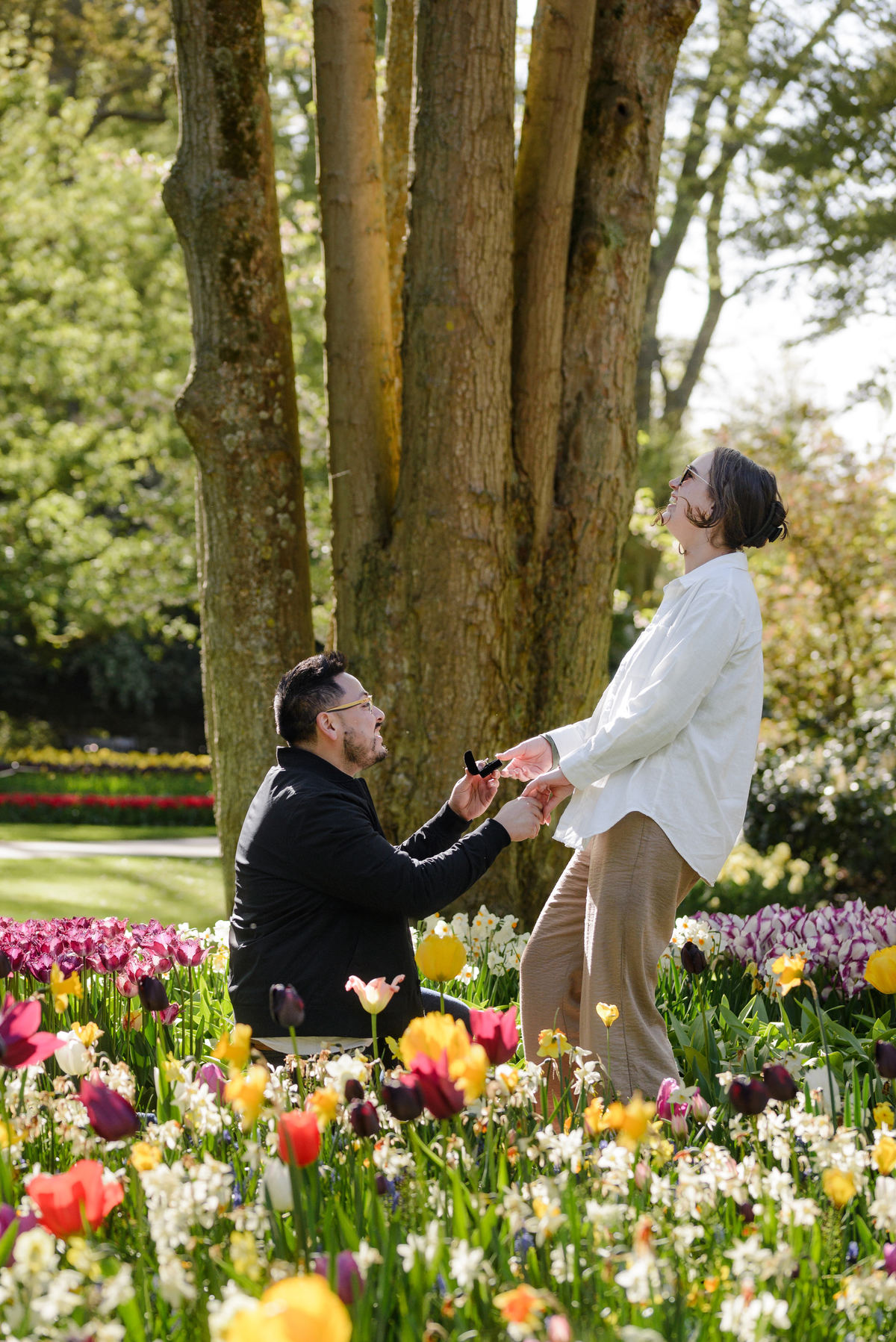 Woman reacting with surprise and joy as her partner proposes among tulips at Keukenhof.