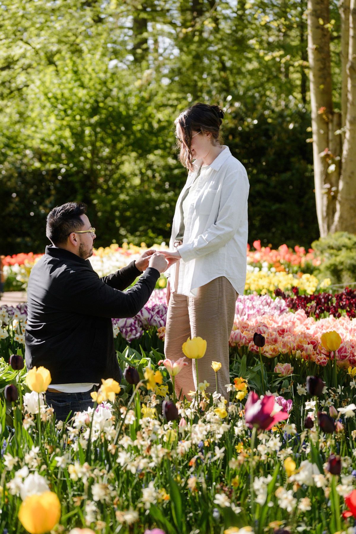 Close-up photograph of a proposal moment with an engagement ring being presented among colorful flowers.