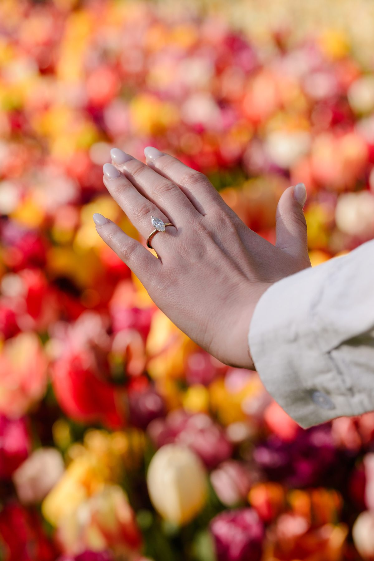 Newly engaged woman showing her engagement ring against a backdrop of vibrant spring flowers.