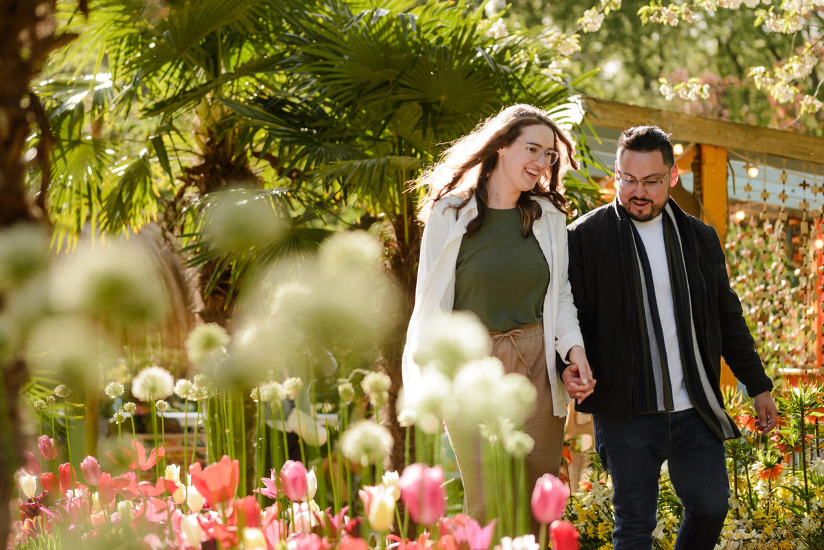 Newly engaged couple walking through Keukenhof Gardens surrounded by spring flowers and greenery.