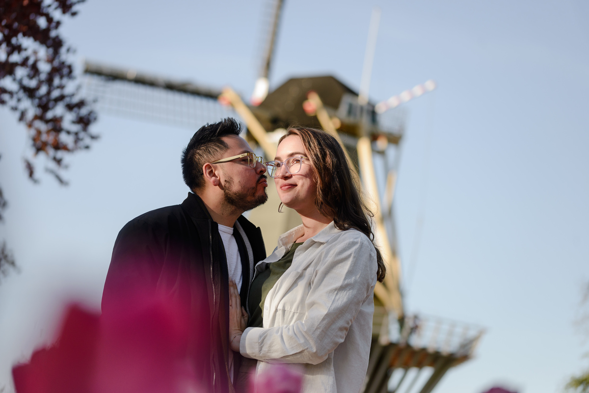 Romantic engagement portrait with a traditional Dutch windmill and tulips in the foreground.