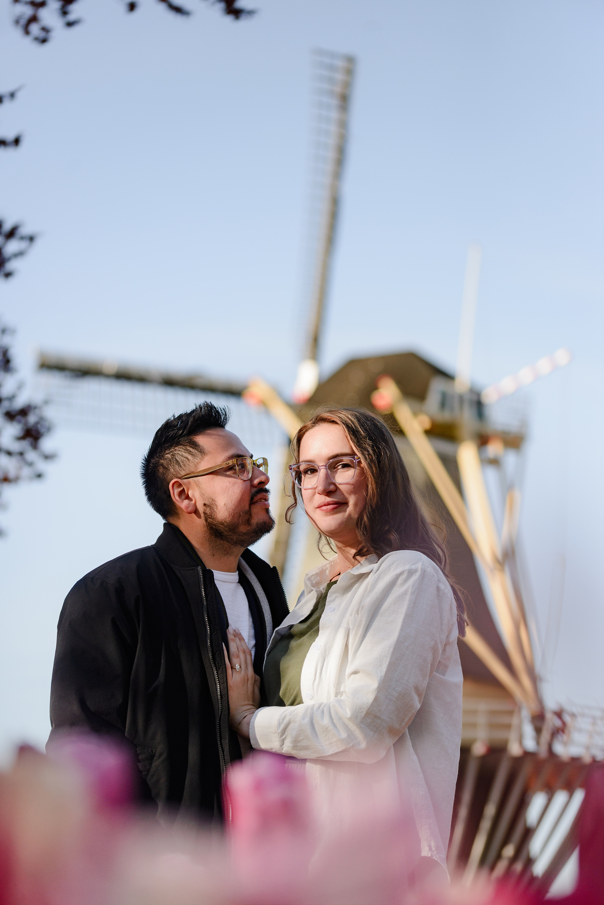 Close engagement portrait with a traditional Dutch windmill in the background at Keukenhof Gardens.