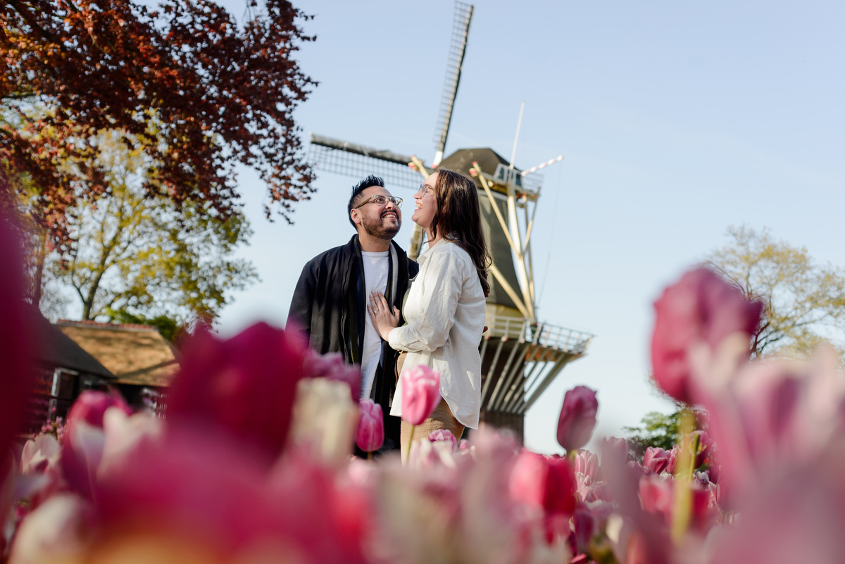 Couple standing near a Dutch windmill surrounded by tulips during an engagement session.