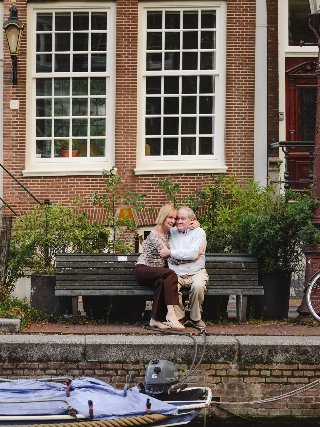 Couple sitting together on a bench beside an Amsterdam canal during a vacation photography session.