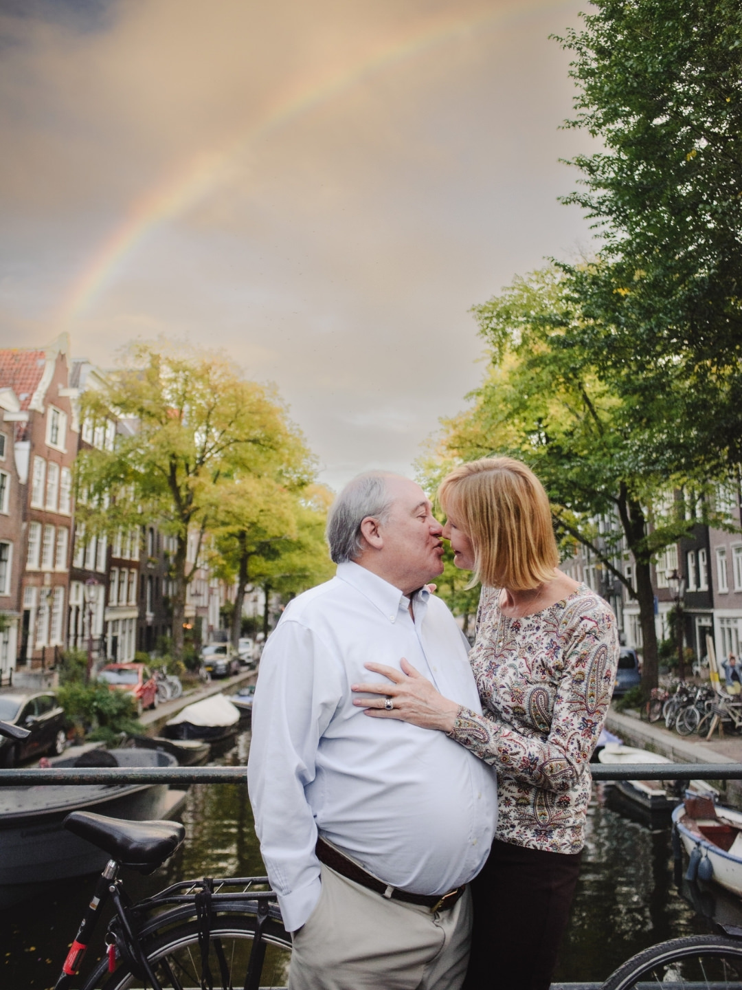 Couple sharing a moment beneath a rainbow over Amsterdam's canals after a summer rain shower.