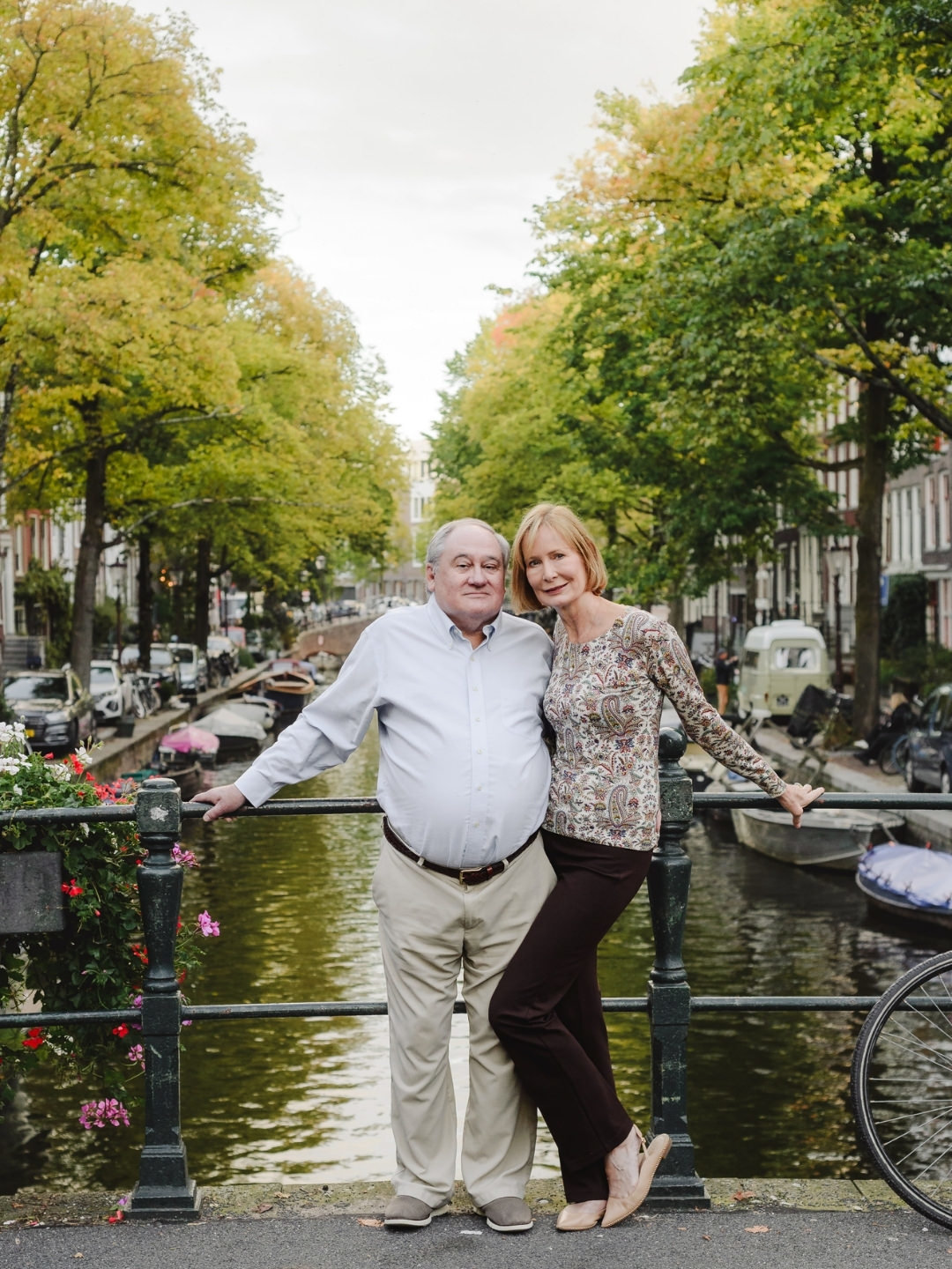 Couple posing on a canal bridge with tree-lined Amsterdam canals in the background.