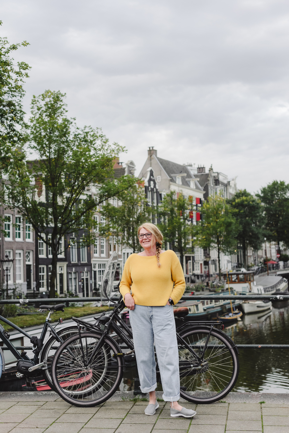 Solo traveler smiling in front of a canal in Amsterdam with beautiful historic houses during her vacation photo session 