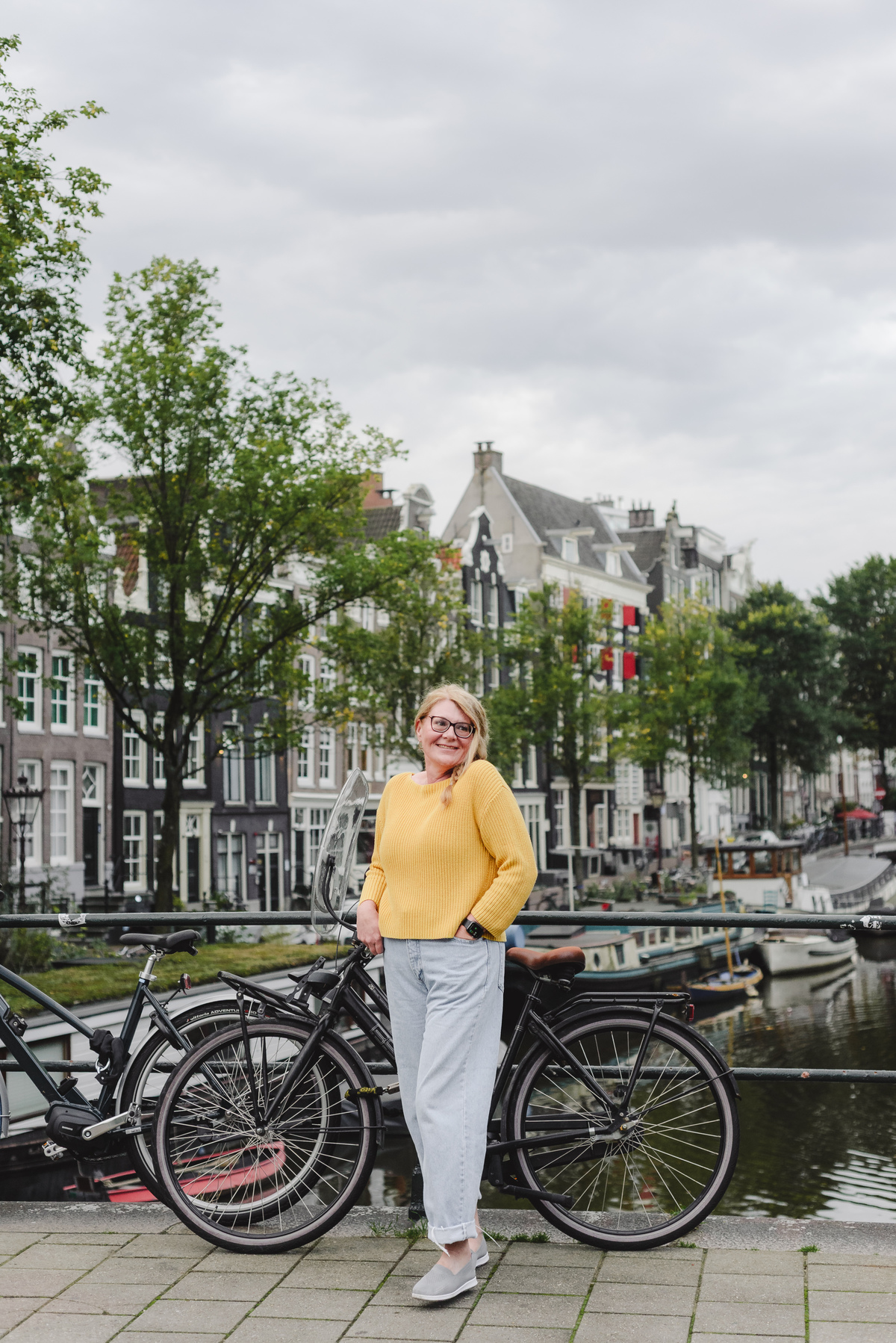 Female solo traveler smiling in front of historical houses and the Singel Canal during her vacation photo session in Amsterdam. 