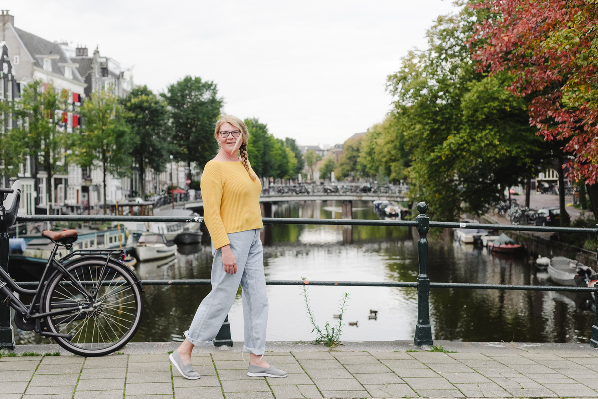 Solo female traveler walking in front of a canal in Amsterdam during her vacation photo session 