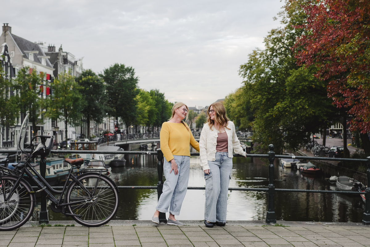 Sisters travelling in Amsterdam and smiling in front of the single canal during her morning vacation photo session. This is a family photography session made over two hours photoshoot in Amsterdam. 