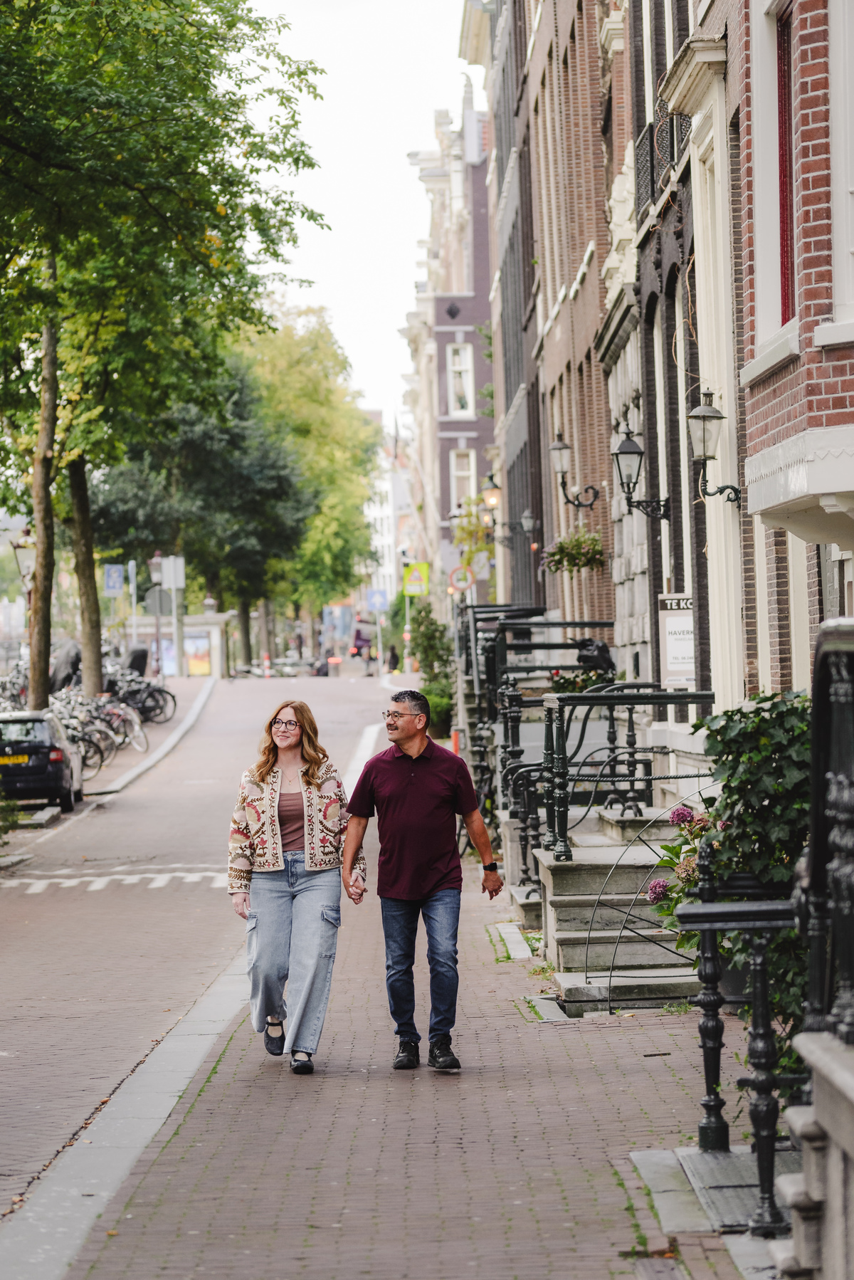 A couple holding hands, walking down the streets of Amsterdam with beautiful historical houses and canals in the background. Vacation photography in Amsterdam 