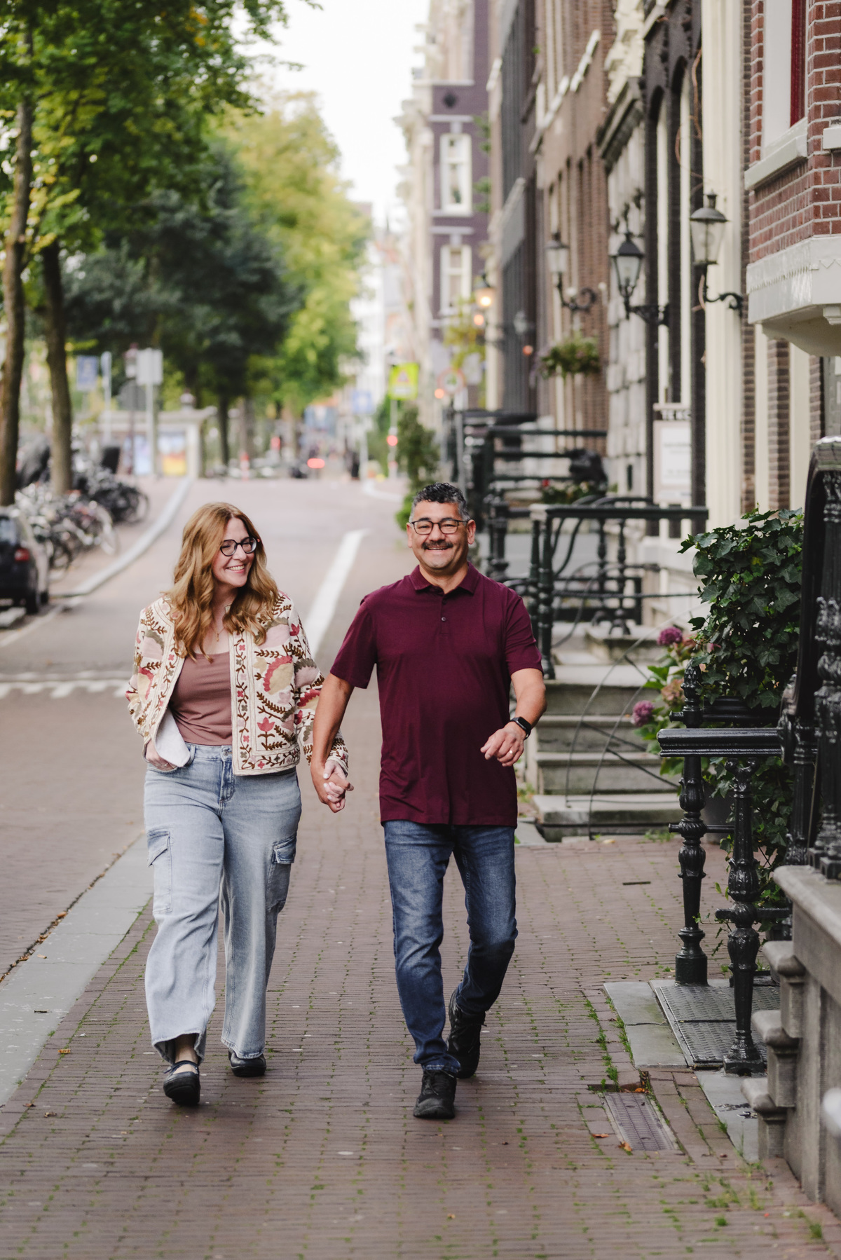A couple holding hands, walking down the streets of Amsterdam with beautiful historical houses in the background. We are capturing the memories of this couple during the morning walk in the city. Vacation Photographer in Amsterdam