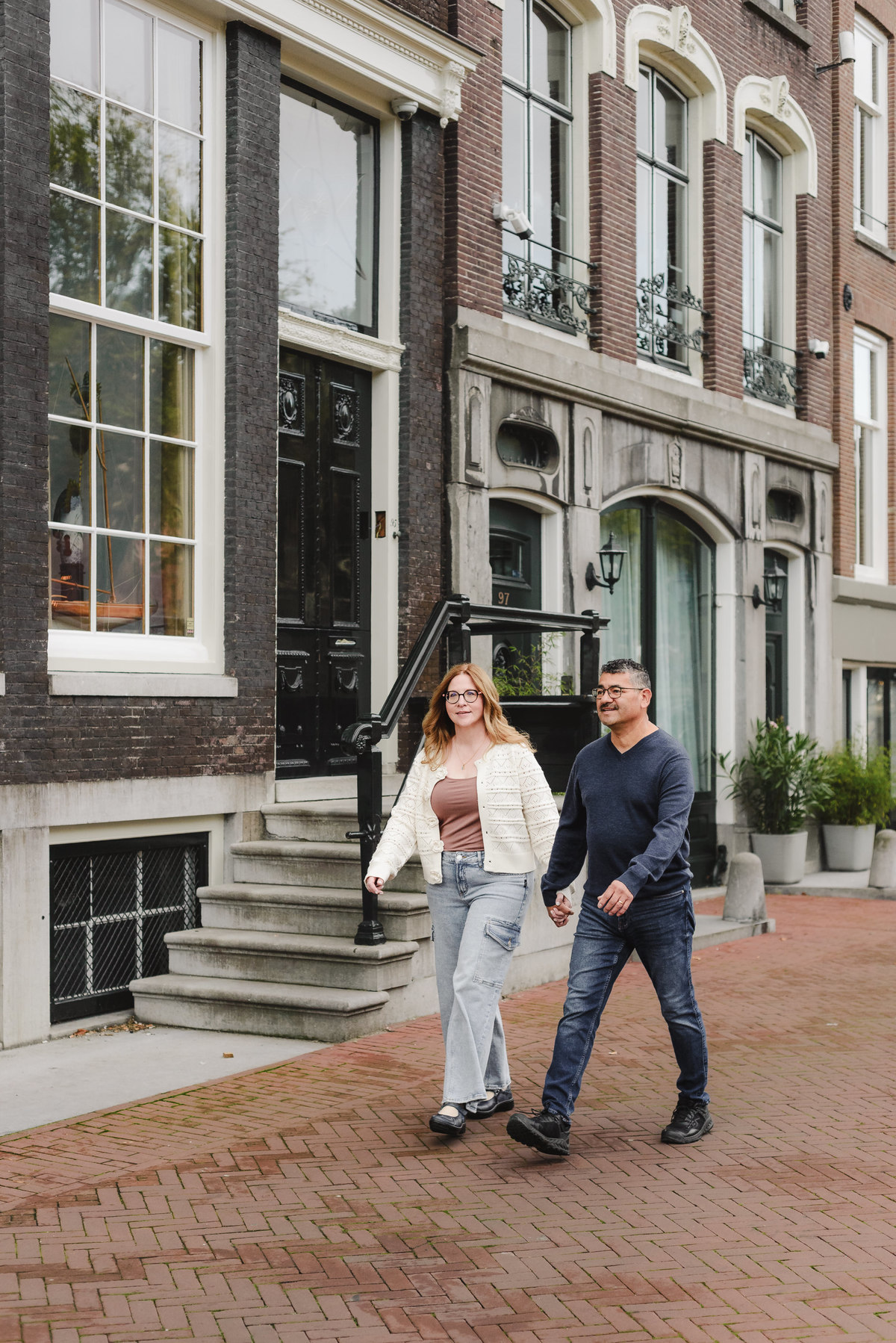 A couple walks hand in hand on the streets of Amsterdam, showing historical façades and beautiful stairs. This is part of the vacation photography session on a quiet morning in Amsterdam. 