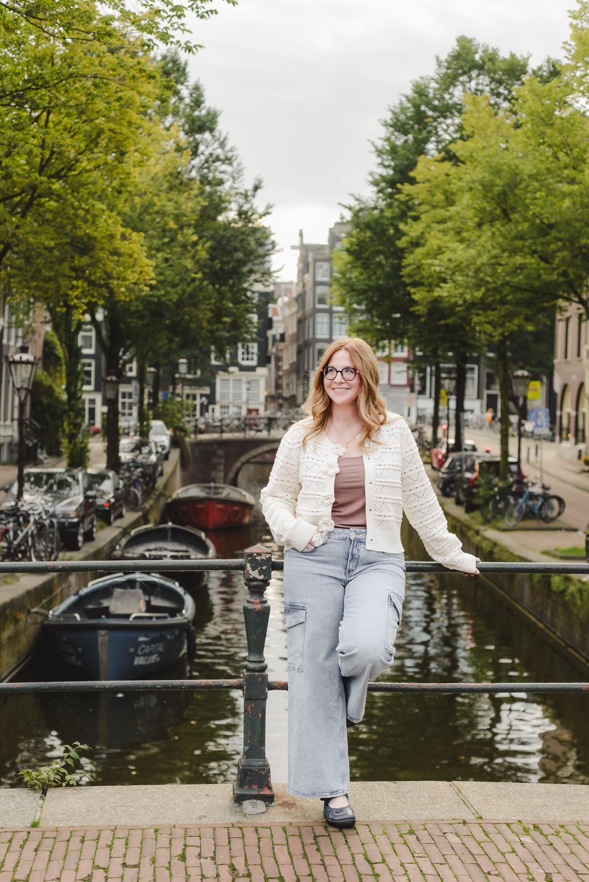 A luxury travel agent boating in front of a canal with historical houses, streets aligned on each side and boats during her morning photo session in Amsterdam. We are capturing business portraits for her travel agency specialising in river cruises 