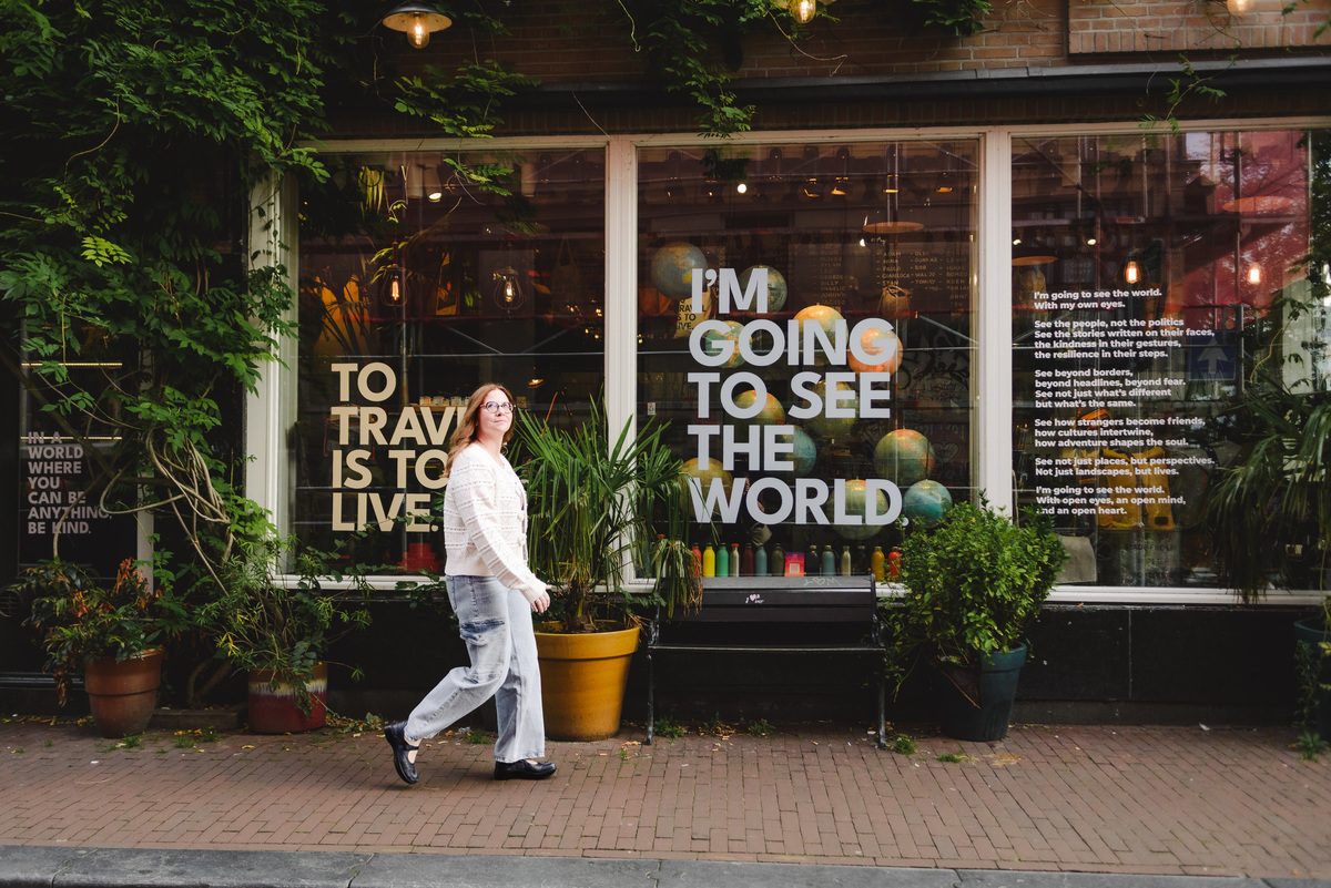 A female travel agent capturing her trip in Amsterdam to show her clients. These pictures will be used on the website and written communication. The background shows a store with messages 