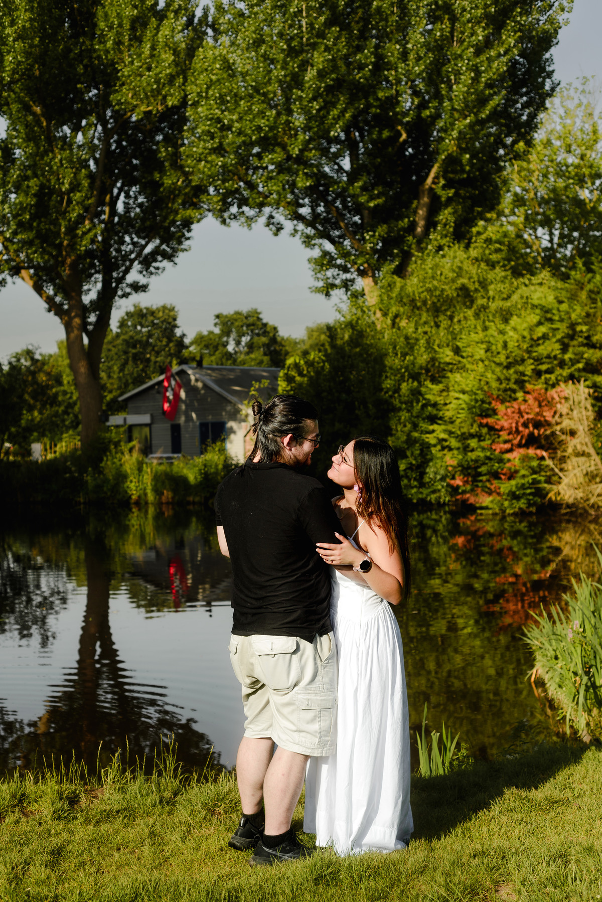 Engaged couple smiling beside a pond in Westerpark.