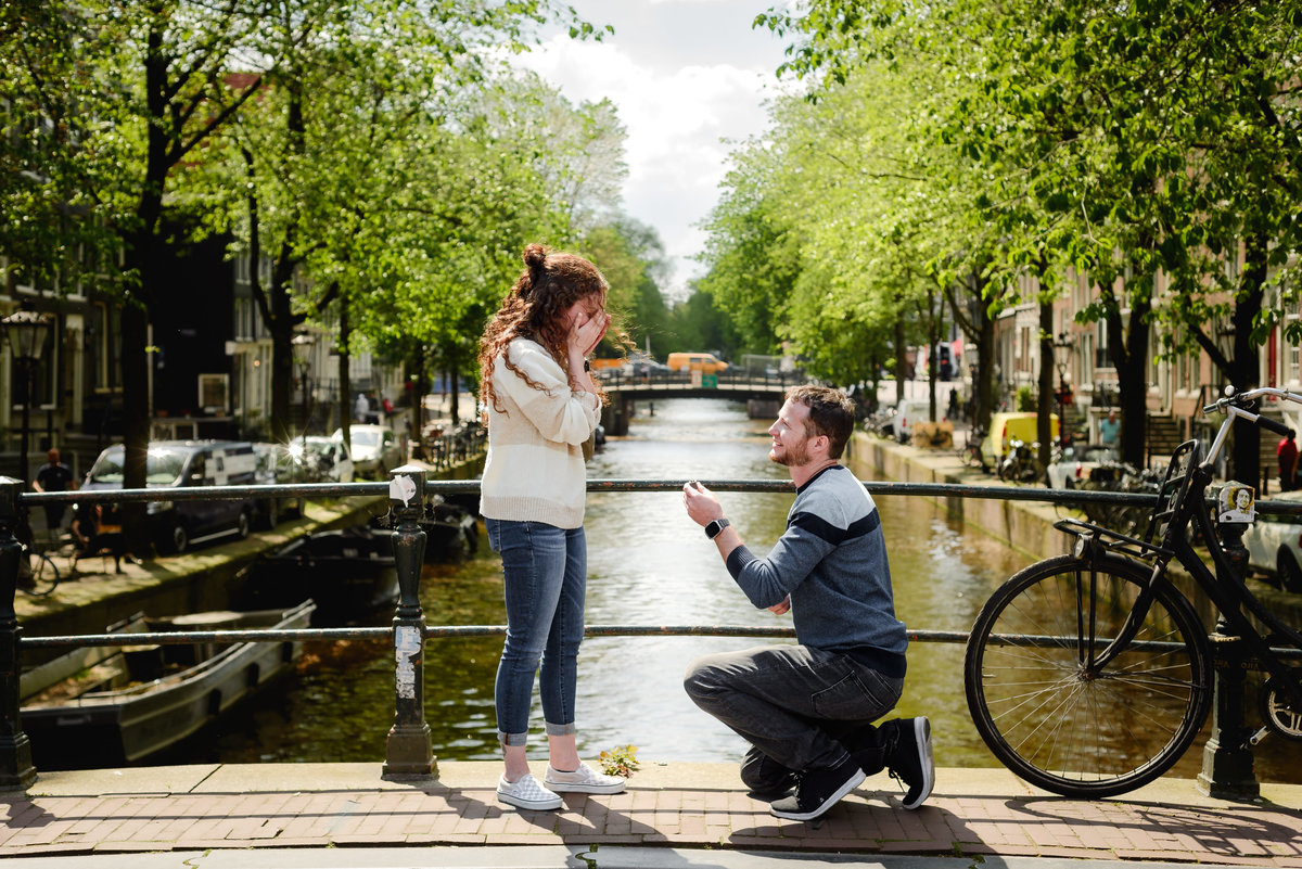 Man proposing on one knee beside an Amsterdam canal during a spring engagement photo session.