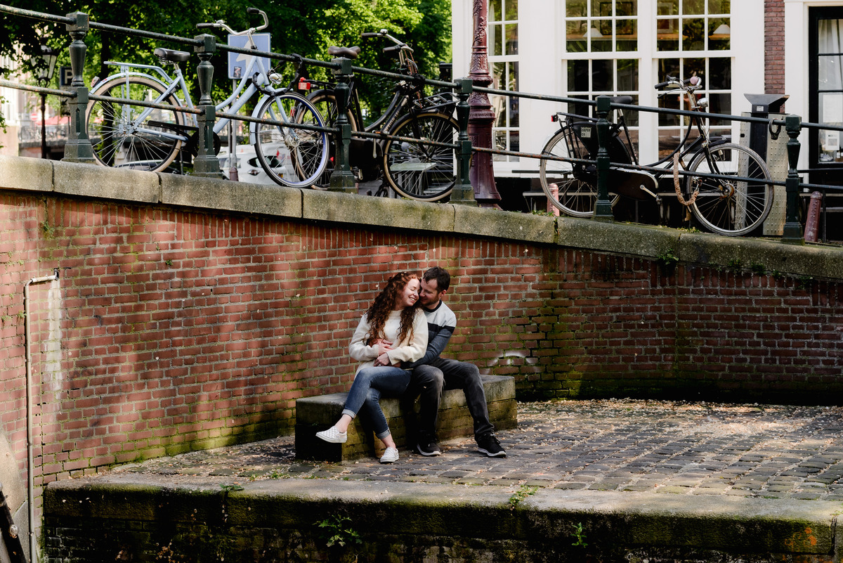 Newly engaged couple sitting together beside an Amsterdam canal after their surprise proposal.
