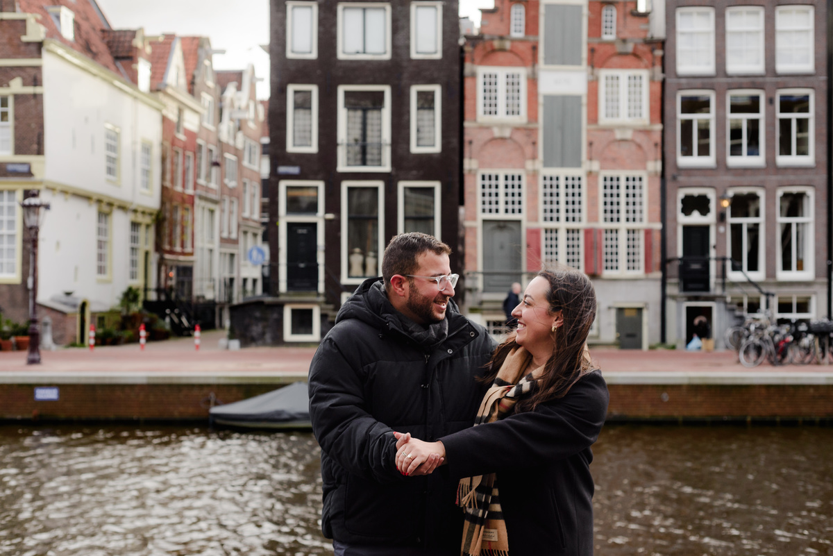 Engaged couple celebrating beside an Amsterdam canal after their surprise proposal.