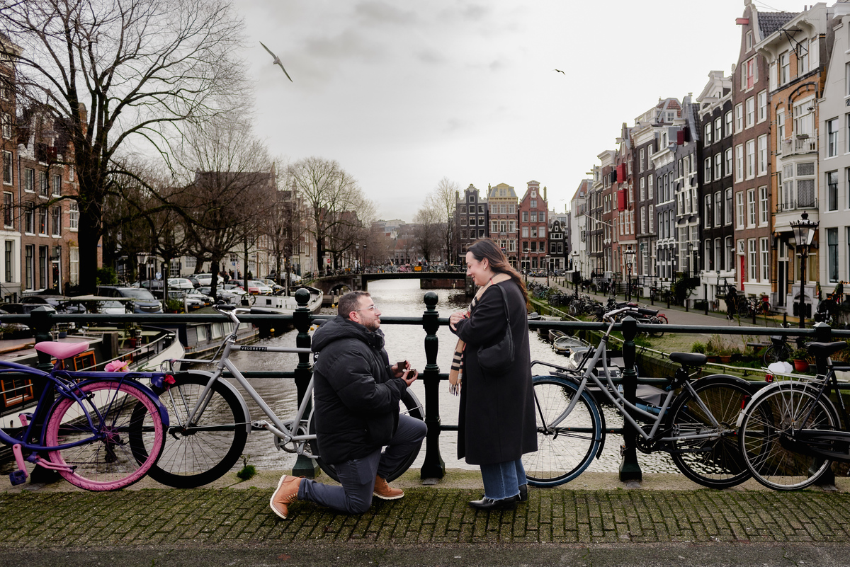 Amsterdam canal proposal with a man on one knee and historic canal houses behind the couple.