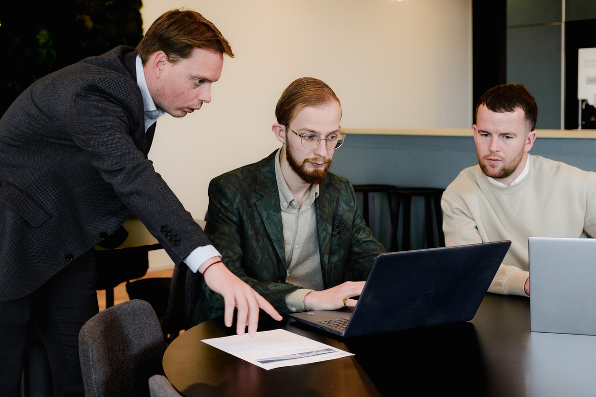 Corporate lifestyle photograph of three colleagues collaborating around a laptop