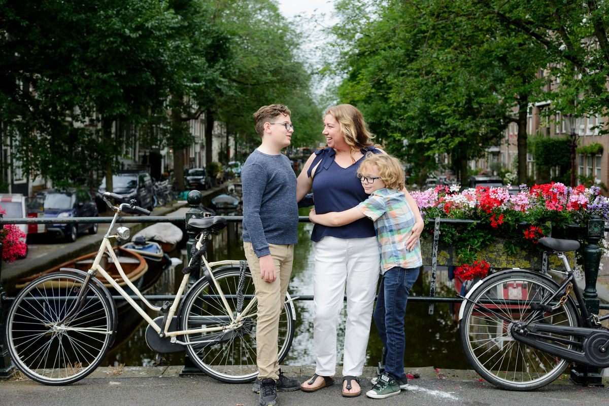 Mother and sons sharing a hug beside a flower-covered canal bridge