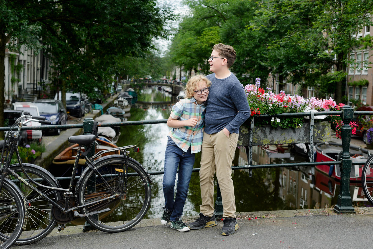 Kids laughing in the Jordaan area in Amsterdam during a photo session. They are in front of a canal with flowers on the bridge. 