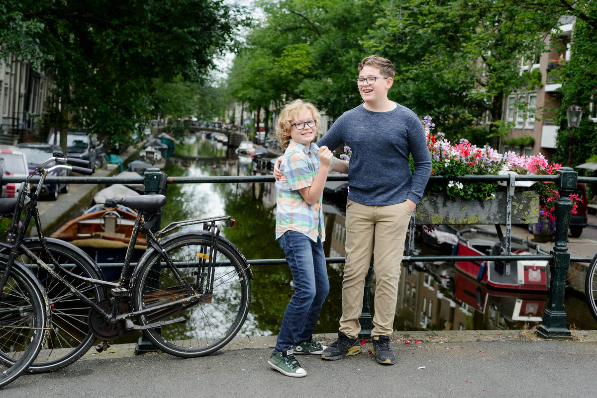 Kids laughing in the Jordaan area in Amsterdam during a photo session. They are in front of a canal with flowers on the bridge. 