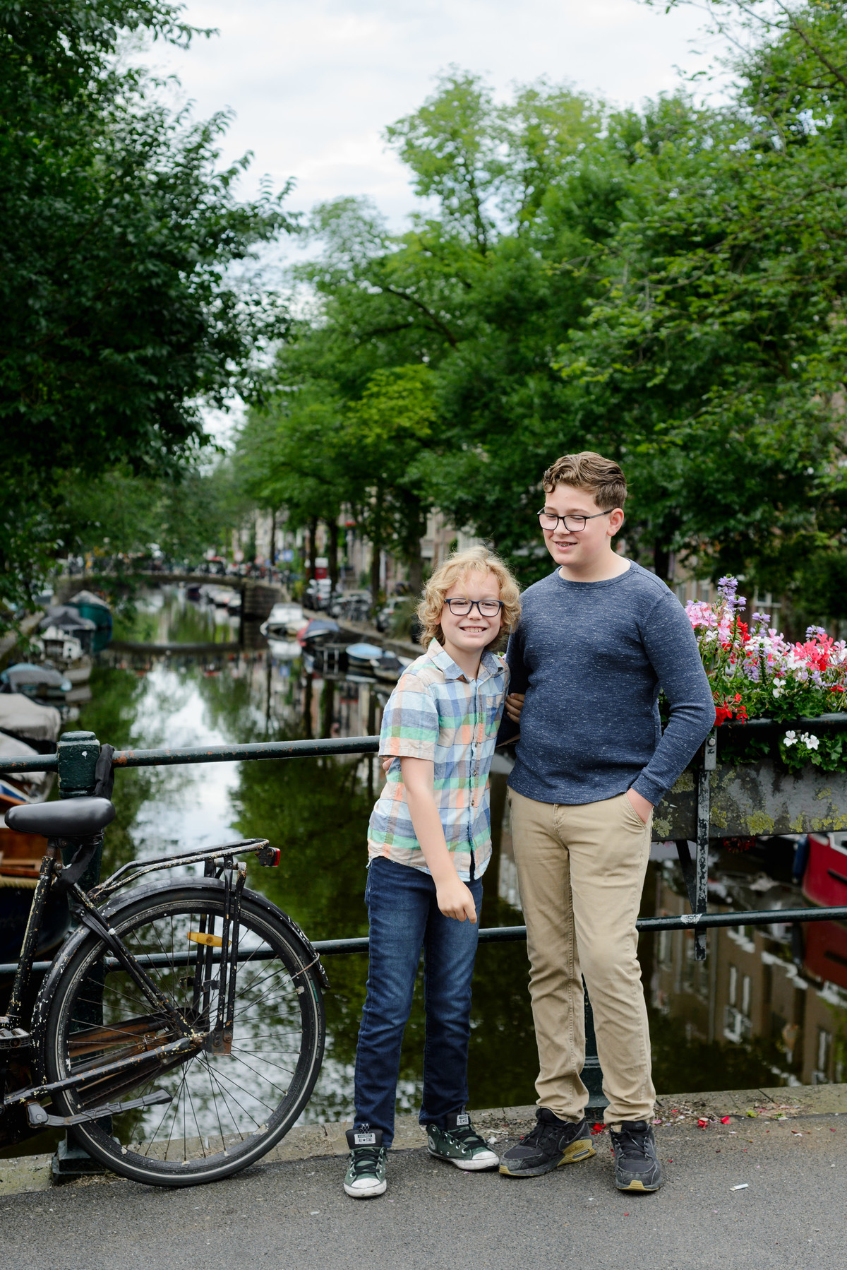 Kids laughing in the Jordaan area in Amsterdam during a photo session. They are in front of a canal with flowers on the bridge. 