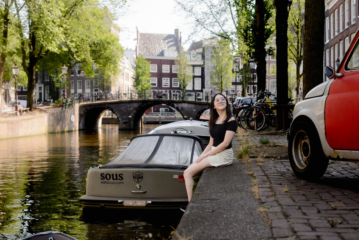 Solo traveller sitting beside the canal with historic Amsterdam houses behind her