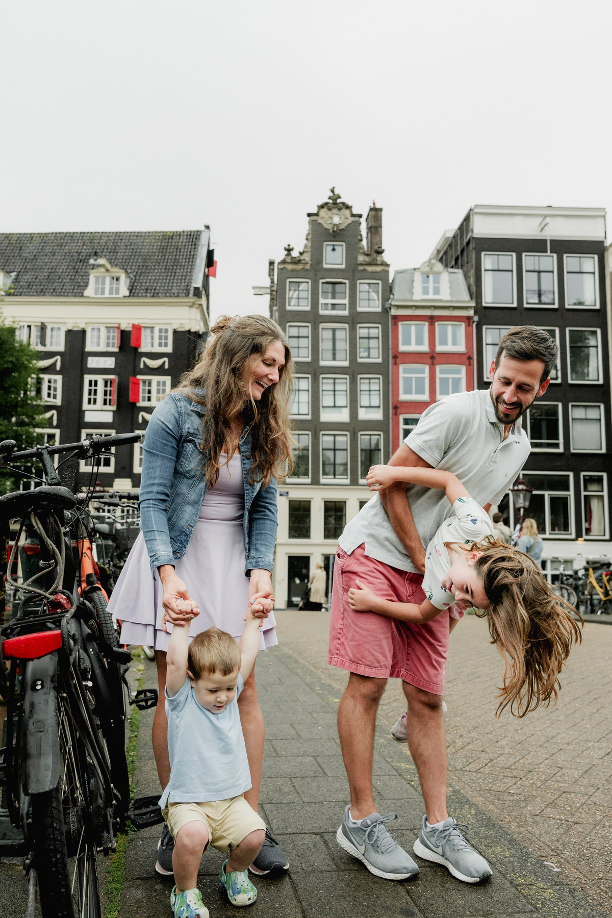Parents playing with their children on a bridge, with Amsterdam houses behind them.