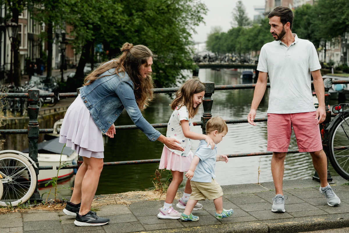 Parents holding their children’s hands as they play together on an Amsterdam bridge.