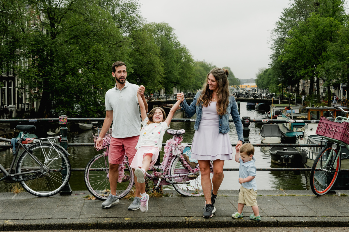 Family holding hands and moving together beside bicycles on an Amsterdam bridge.
