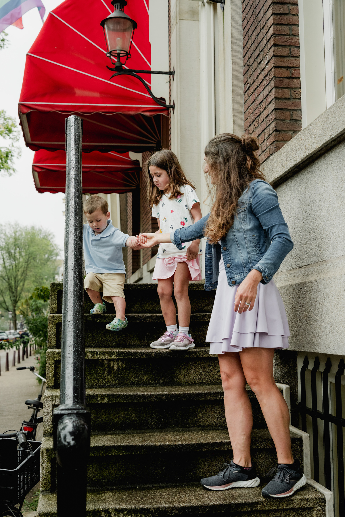 Mother and children pausing on house steps beneath a red awning.