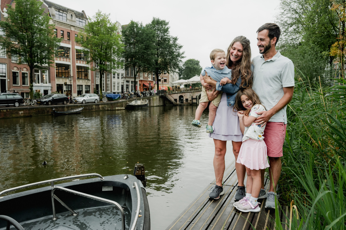 Family standing close together beside the water during their Amsterdam photo session.
