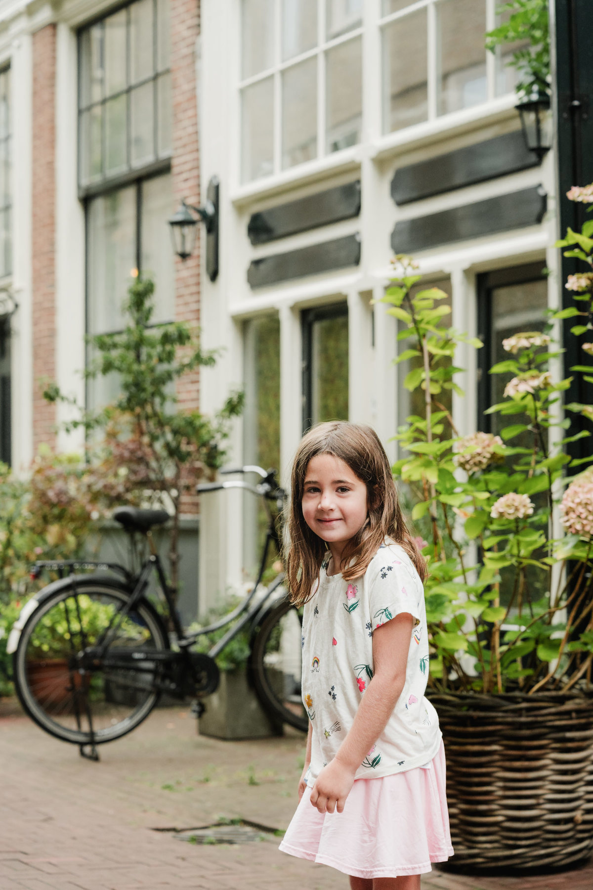 Girl standing on a brick street beside Amsterdam houses and potted plants.
