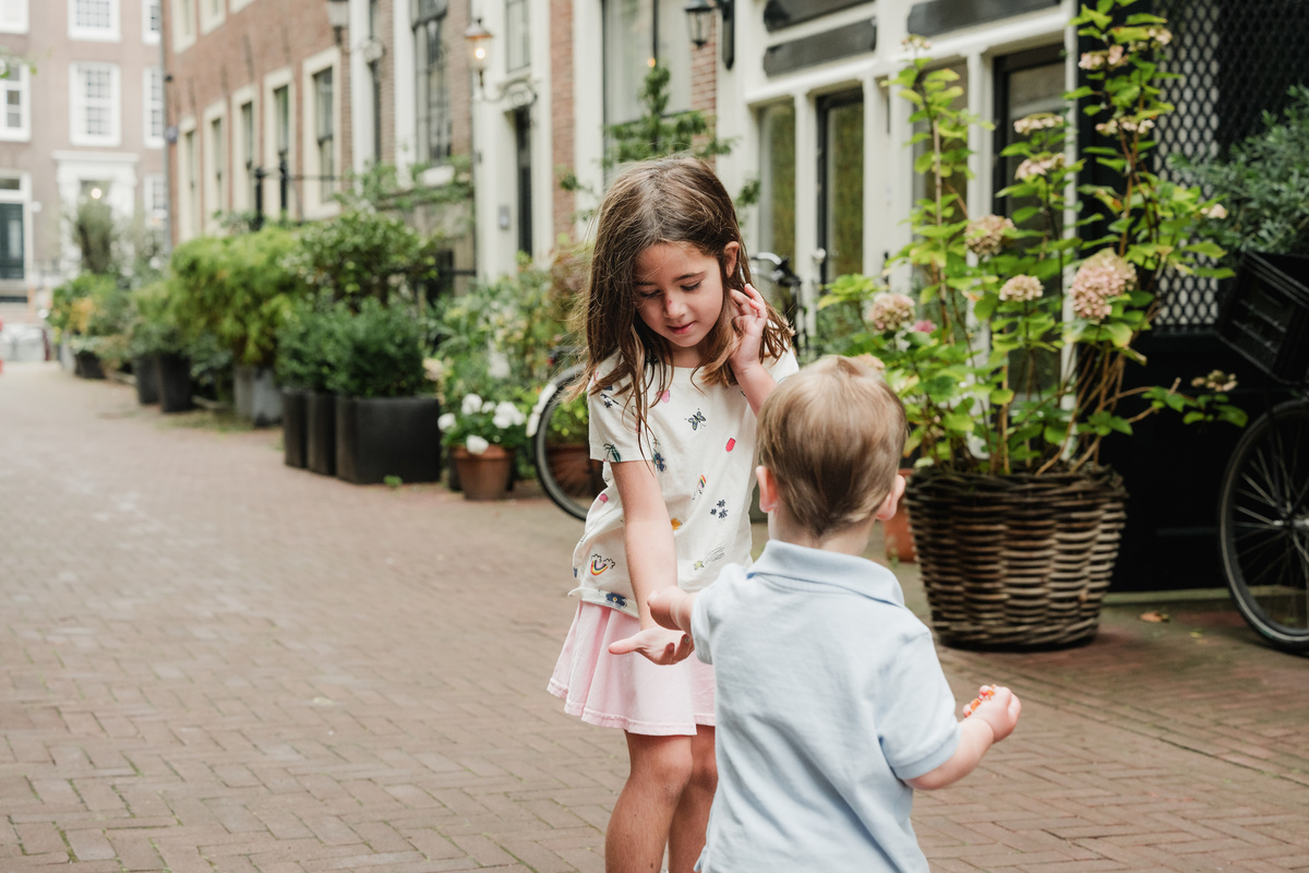 Brother and sister facing each other on a quiet Amsterdam street.